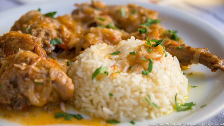 Mound of white rice with chopped herbs surrounded by pieces of braised meat in orange-brown sauce.