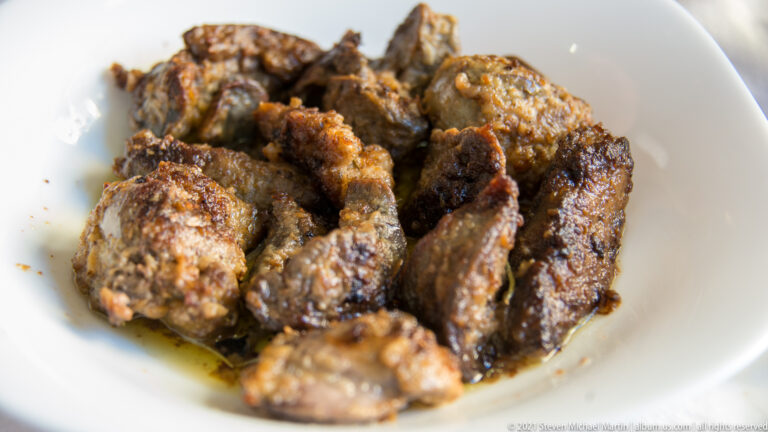 White bowl filled with irregular browned pieces of grilled or pan-fried meat with seasoned, charred surfaces.