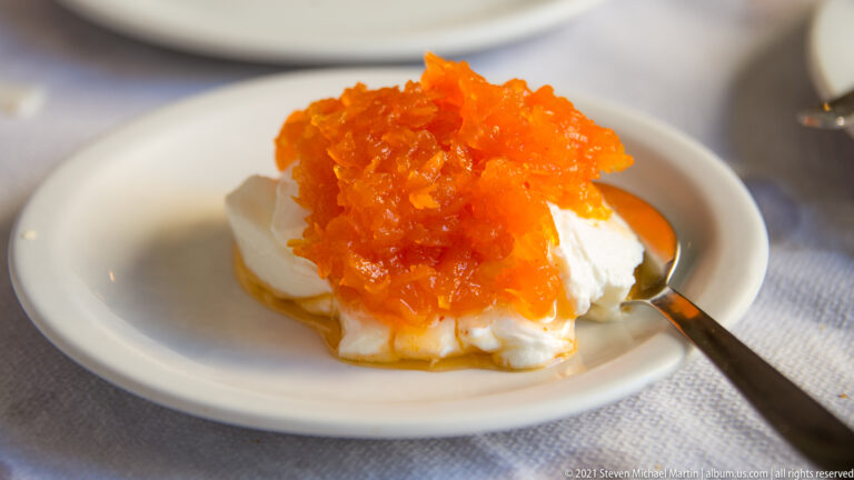Thick white yogurt or fresh cheese topped with bright orange shredded fruit preserve and syrup on a small saucer.