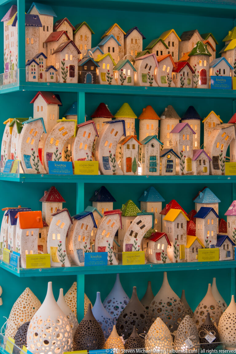 Shelves filled with colorful ceramic miniature houses and perforated pottery displayed in a Cretan souvenir shop.