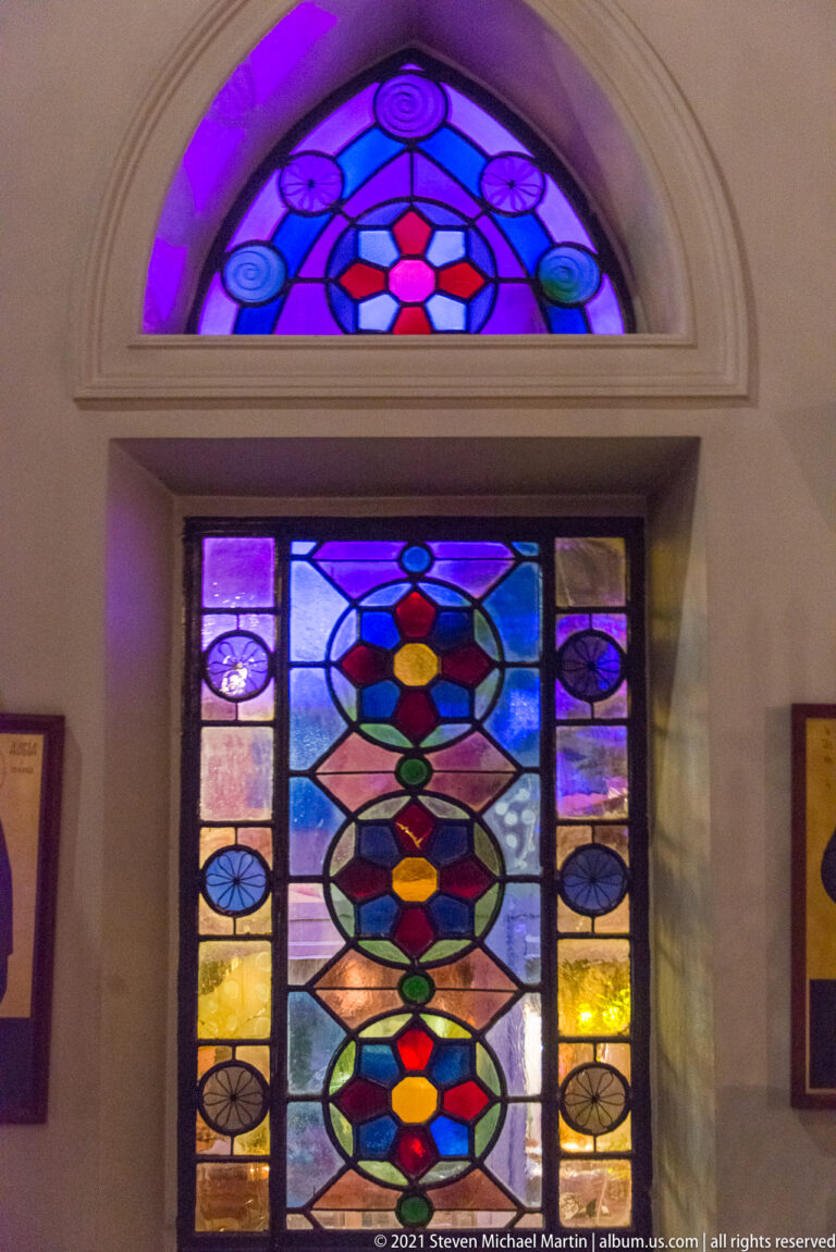 Geometric stained-glass window with circular and diamond patterns in blue, red, green, yellow, and violet inside Saint Titus Church.