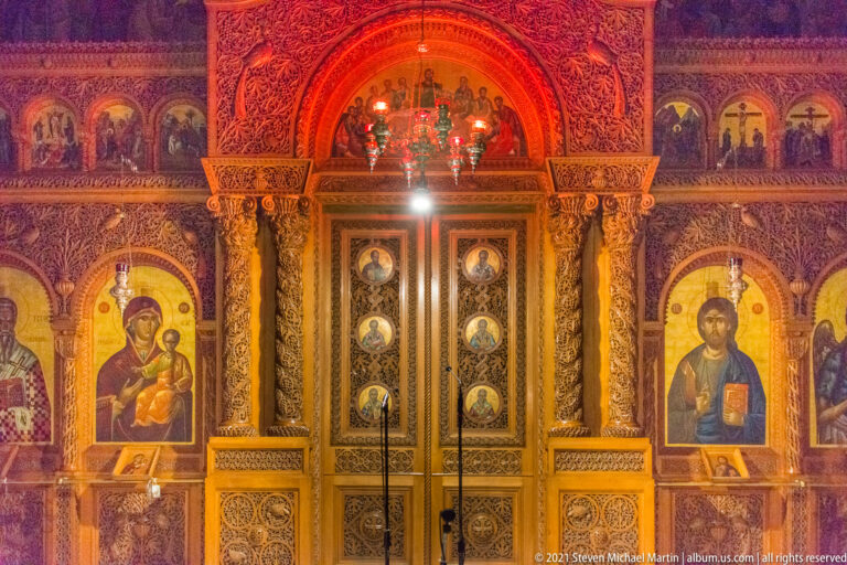 Close frontal view of Saint Titus iconostasis with gilded Royal Doors, icons of the Virgin and Christ, painted panels, and hanging lamp.