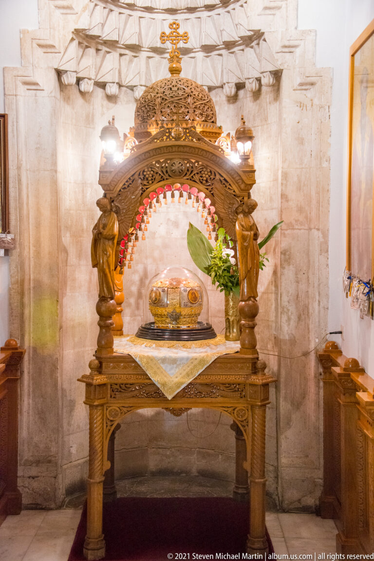 Carved wooden canopy over a silver-toned reliquary on a cloth-covered table, with lamps and flowers inside Saint Titus Church.