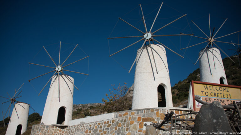 Four whitewashed tower windmills in a hillside row, each with bare radial spars above dark arched openings.
