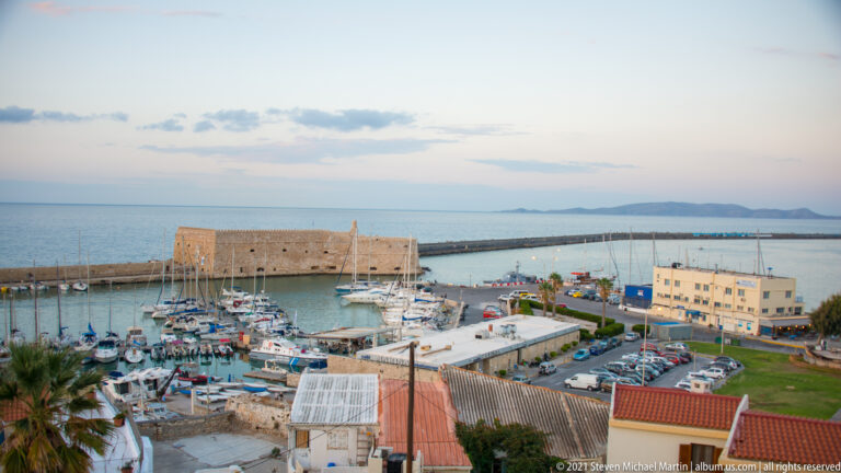 Heraklion marina filled with boats, with the massive stone Koules Fortress at the harbor entrance and sea beyond.