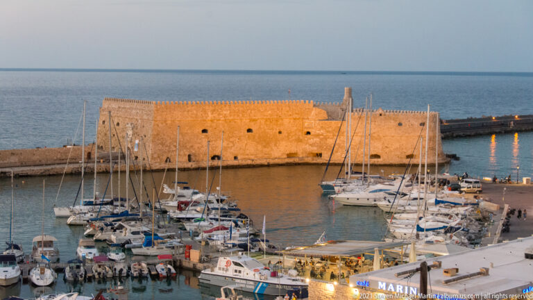 Close elevated view of Koules Fortress behind crowded sailboat masts and moored yachts in Heraklion's marina.