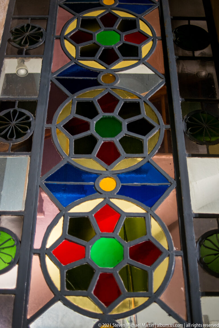 Close detail of circular geometric stained-glass patterns in red, green, blue, yellow, and amber within dark metal framing.