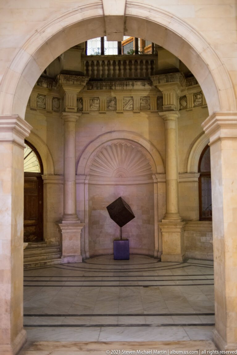 Shell-headed stone niche inside the Heraklion Loggia framed by an arch, with a small dark geometric sculpture on a pedestal.