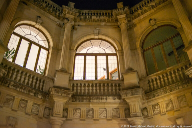 Upward interior view of the Heraklion Loggia with arched windows, curved stone balustrade, columns, and carved brackets.