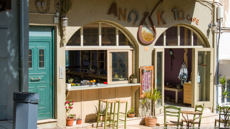 Small arched café storefront with green doors and stools, service counter, potted plants, and handmade signage.