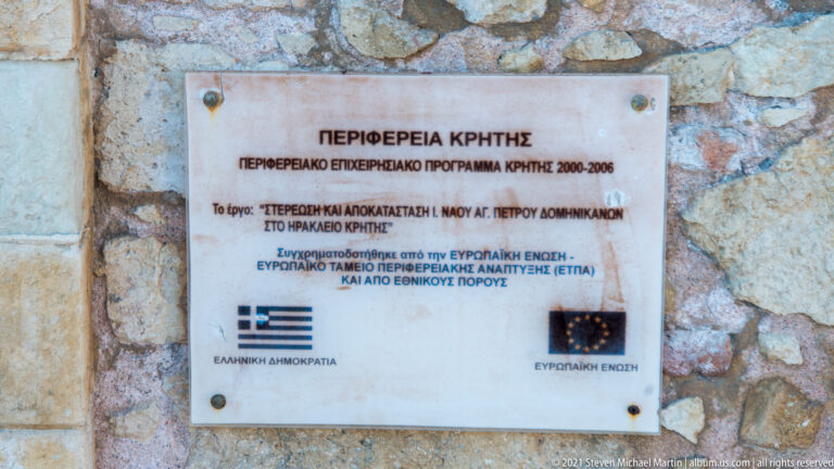 Marble restoration plaque on stone wall with Greek text, Region of Crete heading, and Greek and European Union emblems.