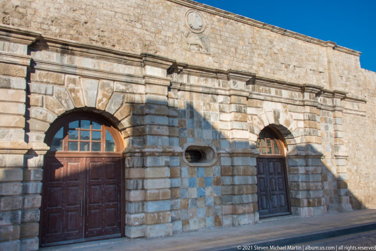 Rusticated Venetian stone façade with two tall arched wooden doors, central oval opening, and small circular feature above.