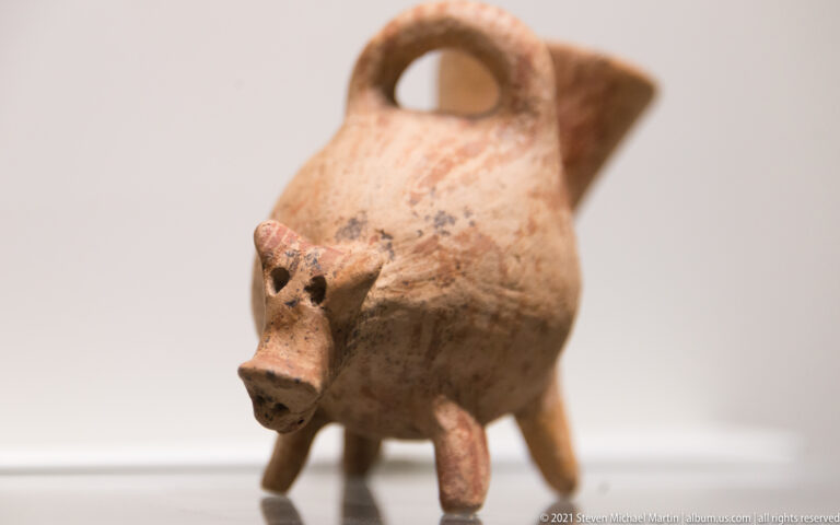 Pig-shaped terracotta vessel with four legs, pointed ears, loop handle, and rear pouring spout.