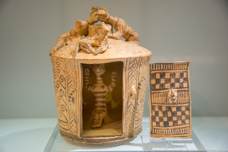 Painted terracotta architectural model with a doorway, standing figure inside, rooftop figures, and a separate patterned panel.
