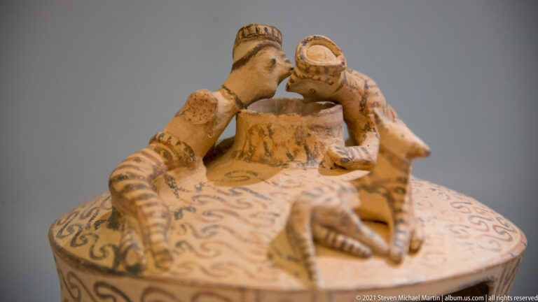 Close view of small terracotta human figures arranged on the roof of a painted miniature structure.