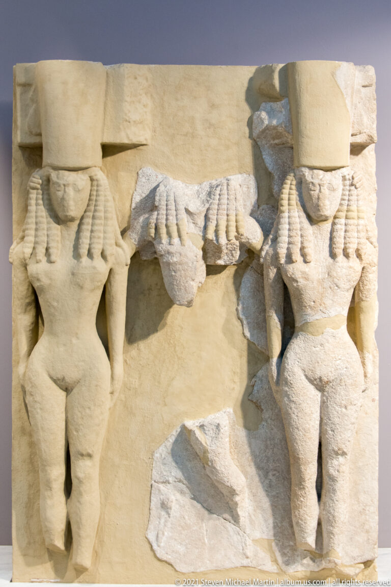 Fragmentary stone architectural relief with two frontal female support figures standing beneath heavy rectangular blocks.