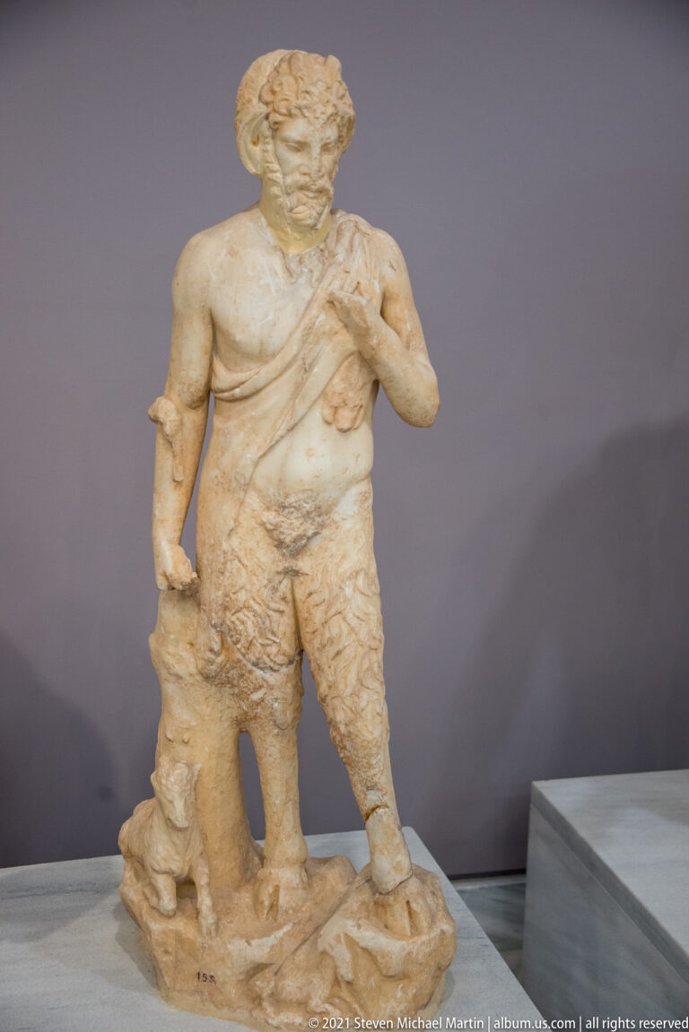 Fragmentary marble statue of a standing bearded male with a draped shoulder, shaggy lower garment, and tree-trunk support.