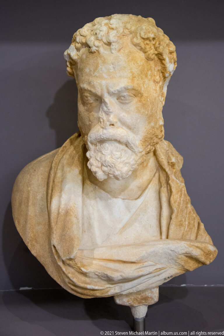 Marble bust of a mature bearded man with short hair and a draped garment across the chest.
