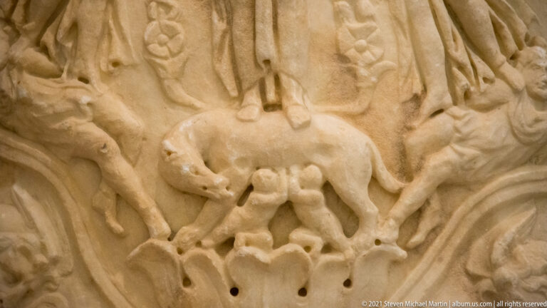 Marble cuirass relief showing a standing she-wolf nursing two small infants beneath her body.