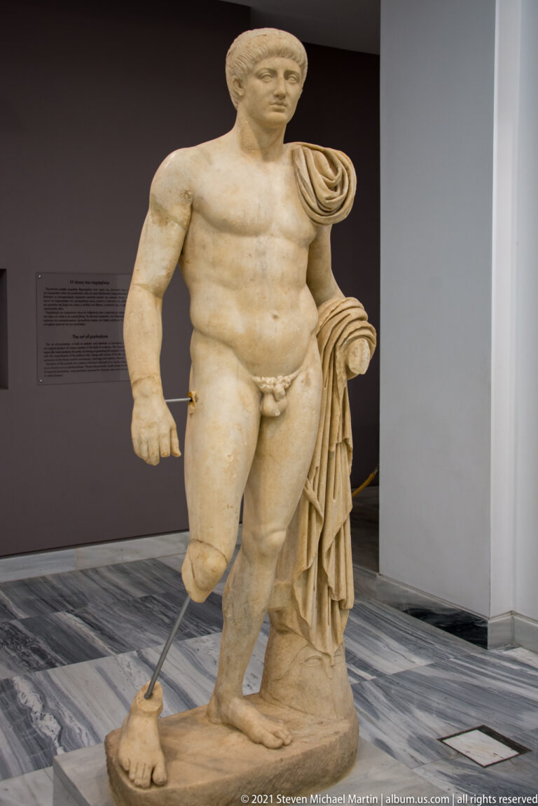 Fragmentary marble statue of a youthful nude male with drapery over one shoulder and a modern support beneath a missing leg.