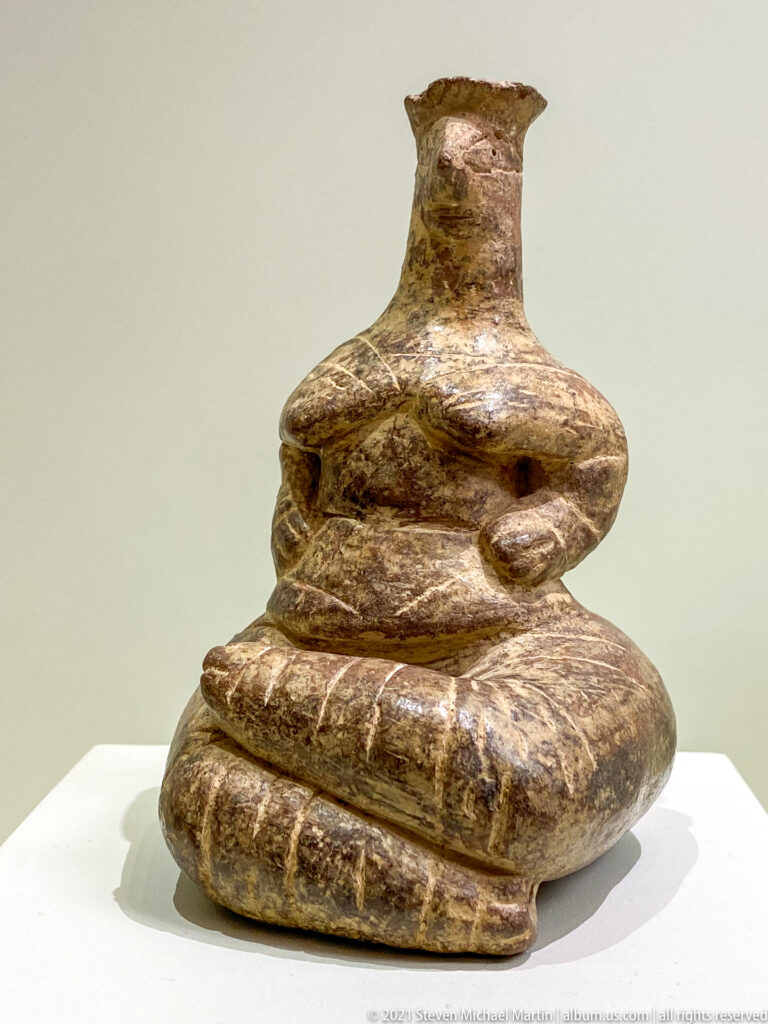 Low mottled stone vessel with stacked rounded lobes, narrow neck, and a short flaring rim.