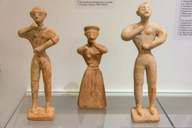 Three terracotta standing human figurines, including a central figure in a long flaring garment.