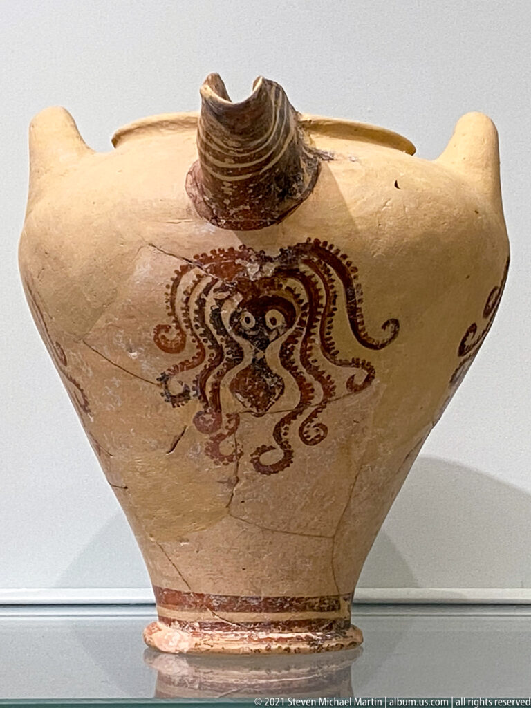 Pale stirrup jar painted with a reddish-brown octopus whose curling tentacles spread across the shoulder and body.