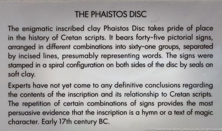 English museum label titled “The Phaistos Disc,” explaining its stamped signs, spiral inscription, undeciphered text, and early seventeenth-century BC date.
