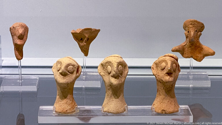 Six terracotta head fragments, including three lower examples with enlarged circular eyes and elongated necks.