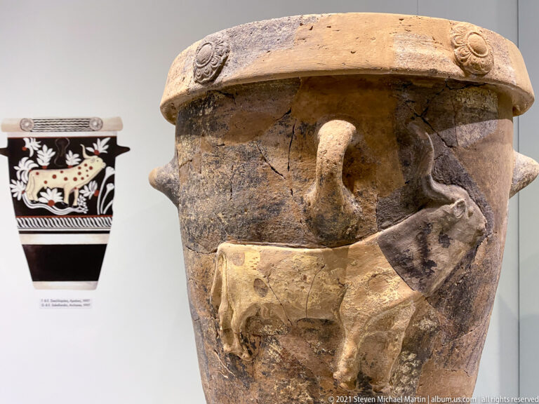 Large reconstructed ceramic storage vessel with an applied animal relief, broad rim, circular impressions, and extensive restored areas.