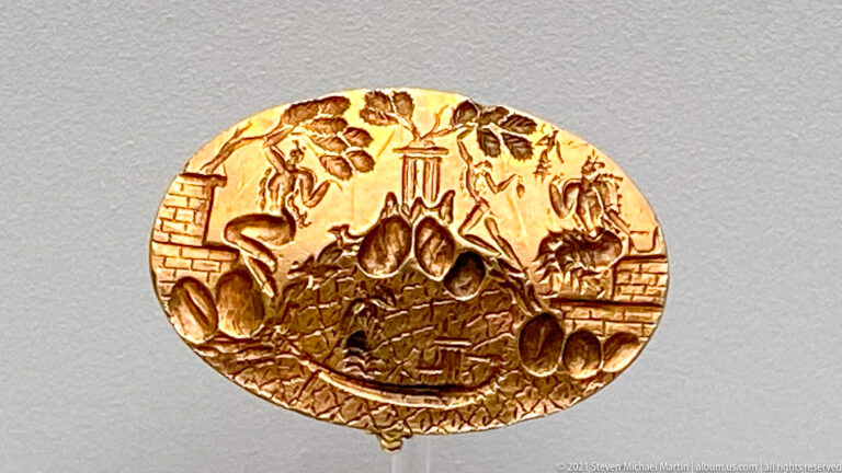 Gold Ring of Minos with engraved figures, sacred trees, architecture, and a deity traveling by boat across a patterned sea.