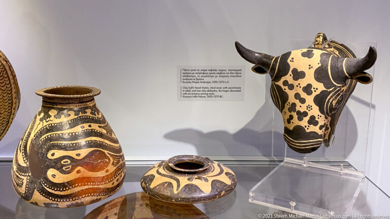 Three dark-ground ceramic objects: a tall painted jar, a low round vessel, and a spotted bull-head form with horns.