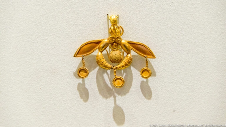 Gold Minoan pendant of two facing bees with open wings, central circular element, and three suspended discs.