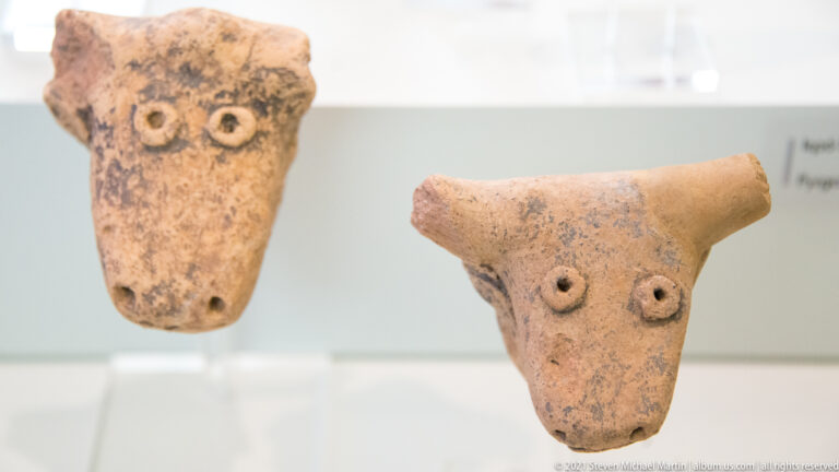 Two small terracotta animal heads with tapered muzzles, applied round eyes, and short side projections.