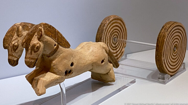 Terracotta horned animal figurine mounted between large disk wheels painted with concentric circles.