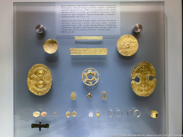 Museum display of gold sheet plaques, embossed strips, star-shaped ornament, rings, and small jewelry fittings.