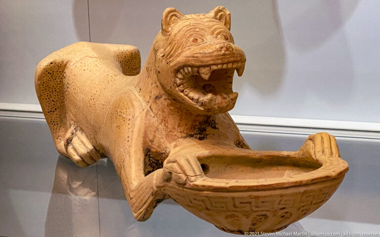 Terracotta lion-shaped vessel with open jaws and forepaws gripping a shallow decorated bowl.