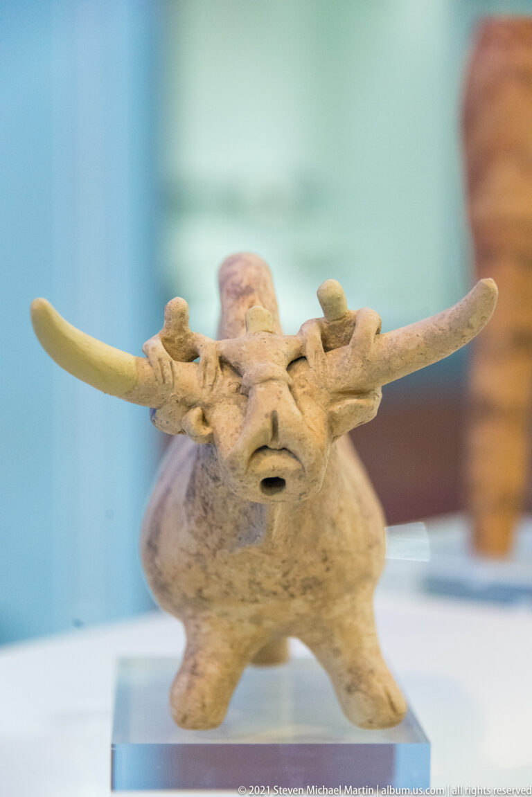 Squat terracotta bull-like object with long lateral horns, modeled face, four legs, and an opening at the muzzle.