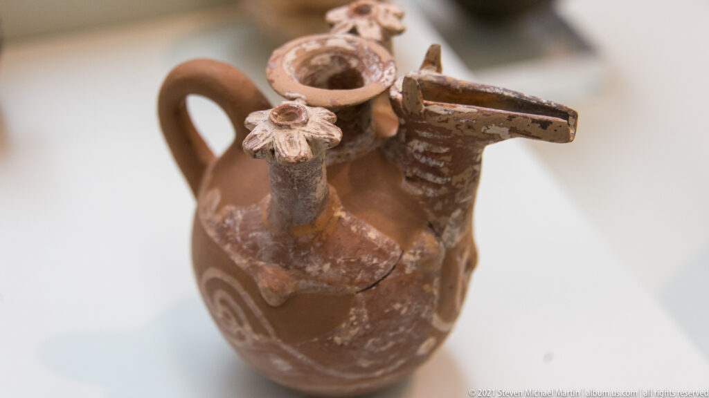 Brown ceramic jug with large handle and several tubular spouts projecting from the neck and shoulder.
