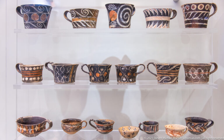 Three rows of small handled ceramic cups decorated with spirals, dots, bands, and other painted motifs.