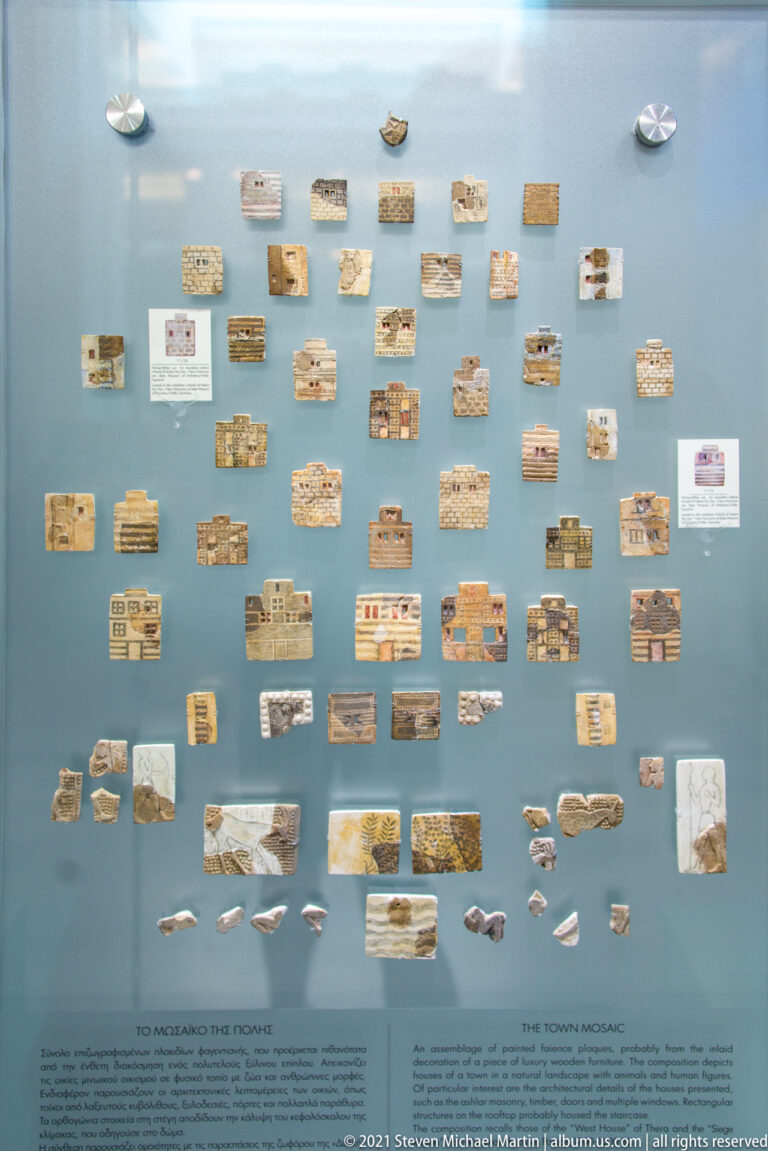 Wall display of dozens of small inscribed clay tablets and fragments arranged in rows with explanatory labels.