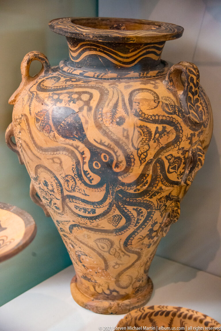 Large Minoan ceramic vessel painted with a dark octopus and other marine motifs across its rounded body.