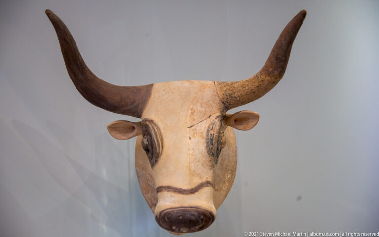 Painted bull-head vessel viewed frontally, with dark curved horns, projecting ears, outlined eyes, and a dark muzzle.