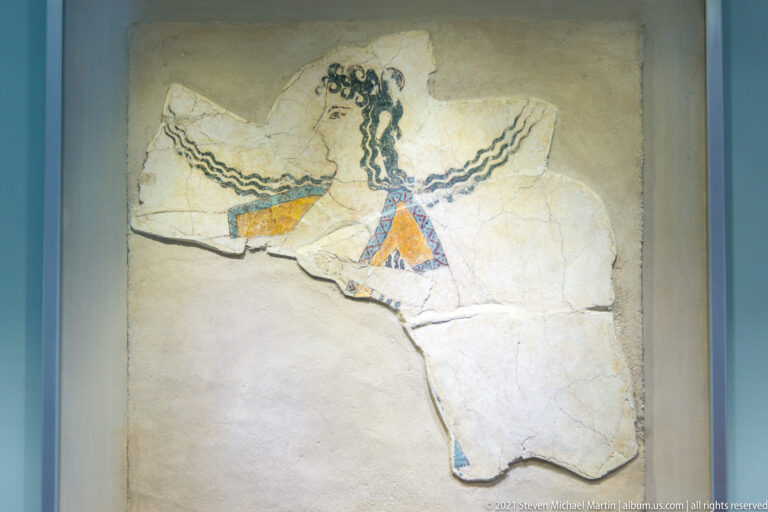 Profile head of the Minoan figure called La Parisienne, with dark curls, red lips, large eye, and sacral knot.
