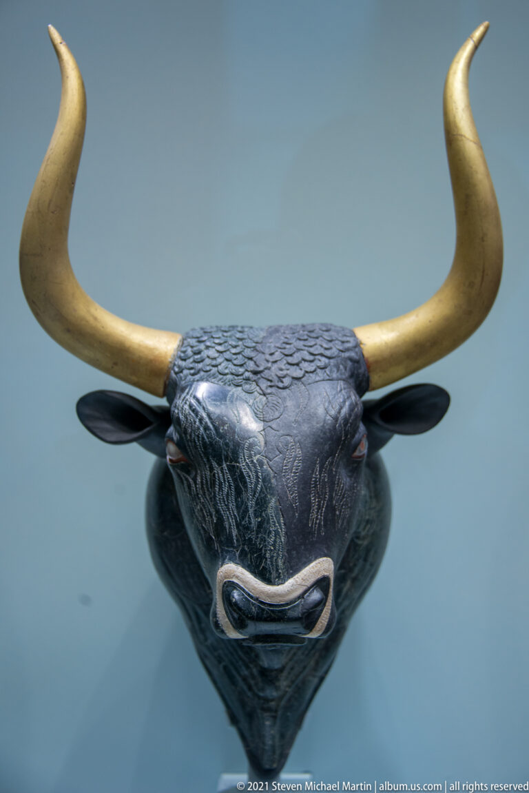Stone Bull’s-head rhyton from Knossos with restored horns, inlaid eye, modeled muzzle, and incised hair.