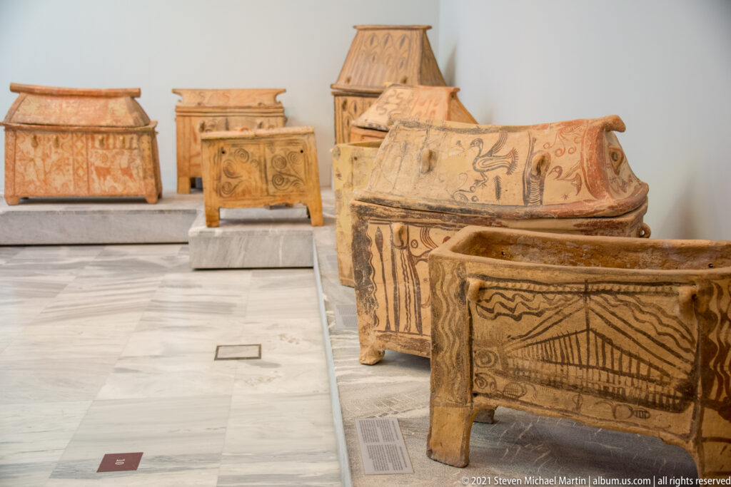 Several painted terracotta larnakes displayed in a row, with short legs, lids, and geometric or figural decoration.