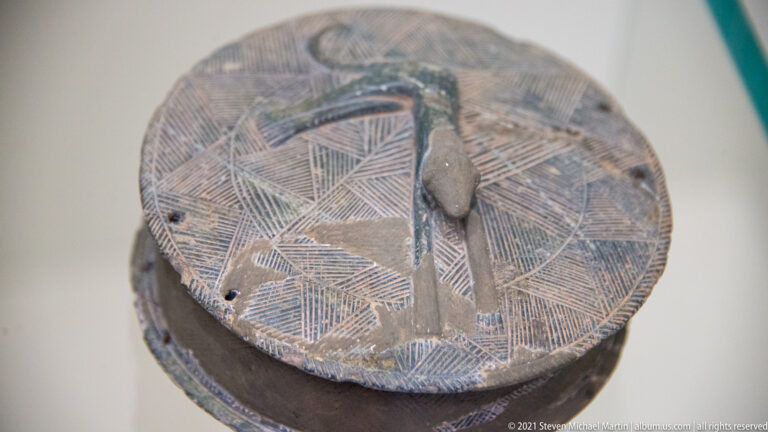 Circular dark lid with dense crosshatched triangular incisions and a raised central fastening.