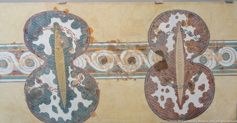 Reconstructed Minoan fresco with two large stylized plant motifs and a horizontal border of rosettes and circular designs.