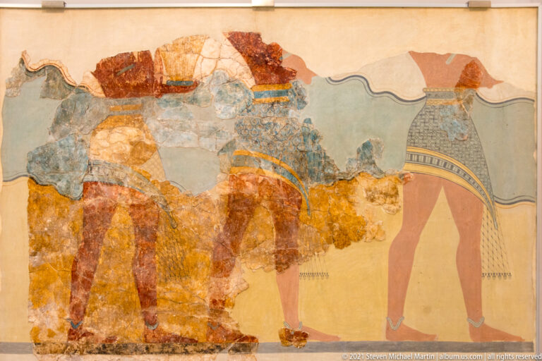 Fragmentary Minoan fresco with several male figures walking in procession across a pale blue-green background.