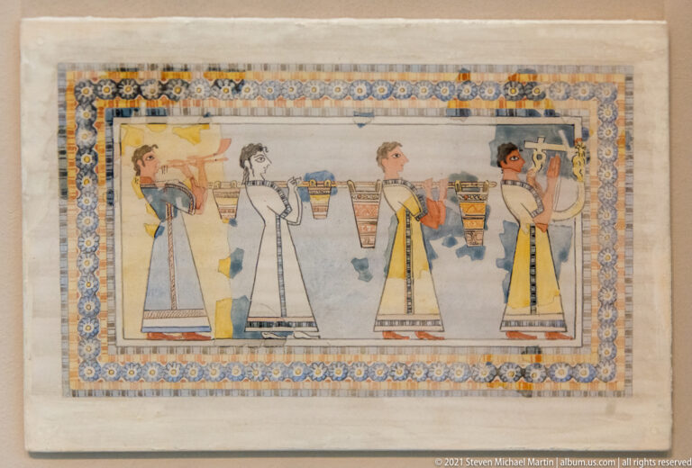 Reconstructed Minoan fresco showing four women in long garments carrying vessels in procession within a decorative border.